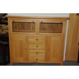 A large modern cabinet made oak unit, with glazed drop down panel doors above a lower section fitted