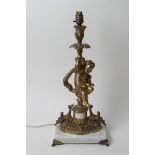 A gilt metal table lamp in the form of a cherub and raised on a squared white marble base.