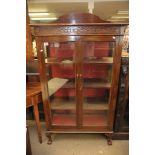 An Edwardian two door glazed display cabinet fitted with four shelves and raised on claw and ball
