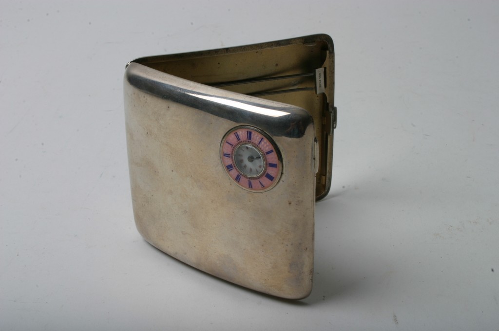 A silver cigarette case inset with a pink enamelled watch face,
