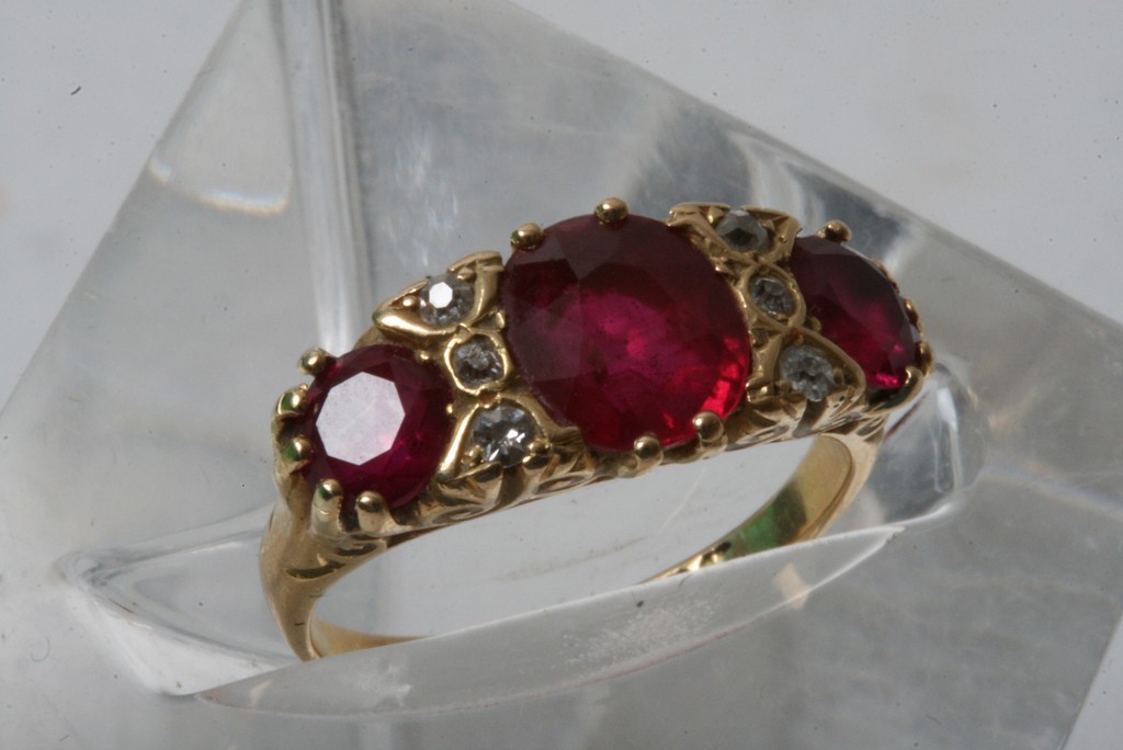 An 18ct gold ring inset with central band of three large rubies flanked by two rows of diamonds