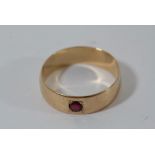A gold wedding band ring set with single red stone
