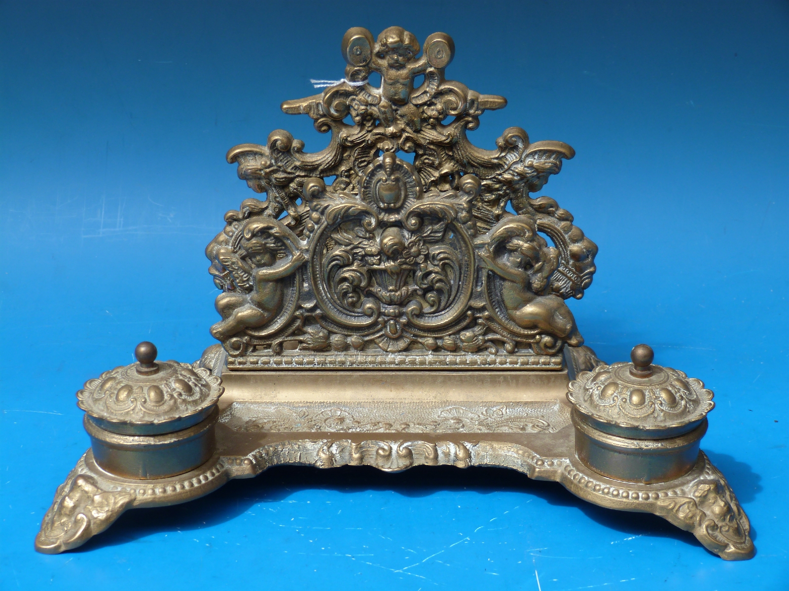 An ornate brass desk tidy with lined hinged inkwells raised on ornate scrolling feet