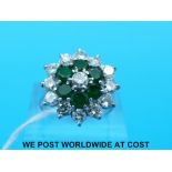 A white metal ring marked 18ct set with a round brilliant cut diamond surrounded by six emeralds,