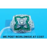 An 18ct white gold ring set with a round cut diamond surrounded by emeralds and a further row of