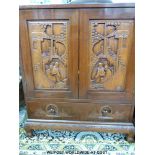 A Chinese elm desk with carved door panels to the cupboard depicting a couple by pergoda over