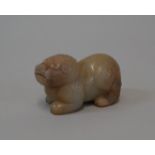 A Chinese carved celadon jade recumbent lion dog, with square aperture through back, 6.4cm long.