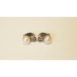 A pair of unmarked white metal earrings set large cultured pearl above a baguette and round cut