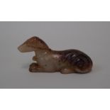 A Chinese carved celadon and russet jade recumbent hound, Qing, realistically carved, 9cm long.