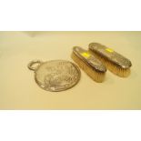 A sterling silver ciruclar hand mirror; together with two silver backed clothes brushes.
