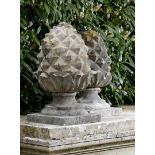 A pair of carved stone gatepier pineapple finials  19th century on later composition stone bases