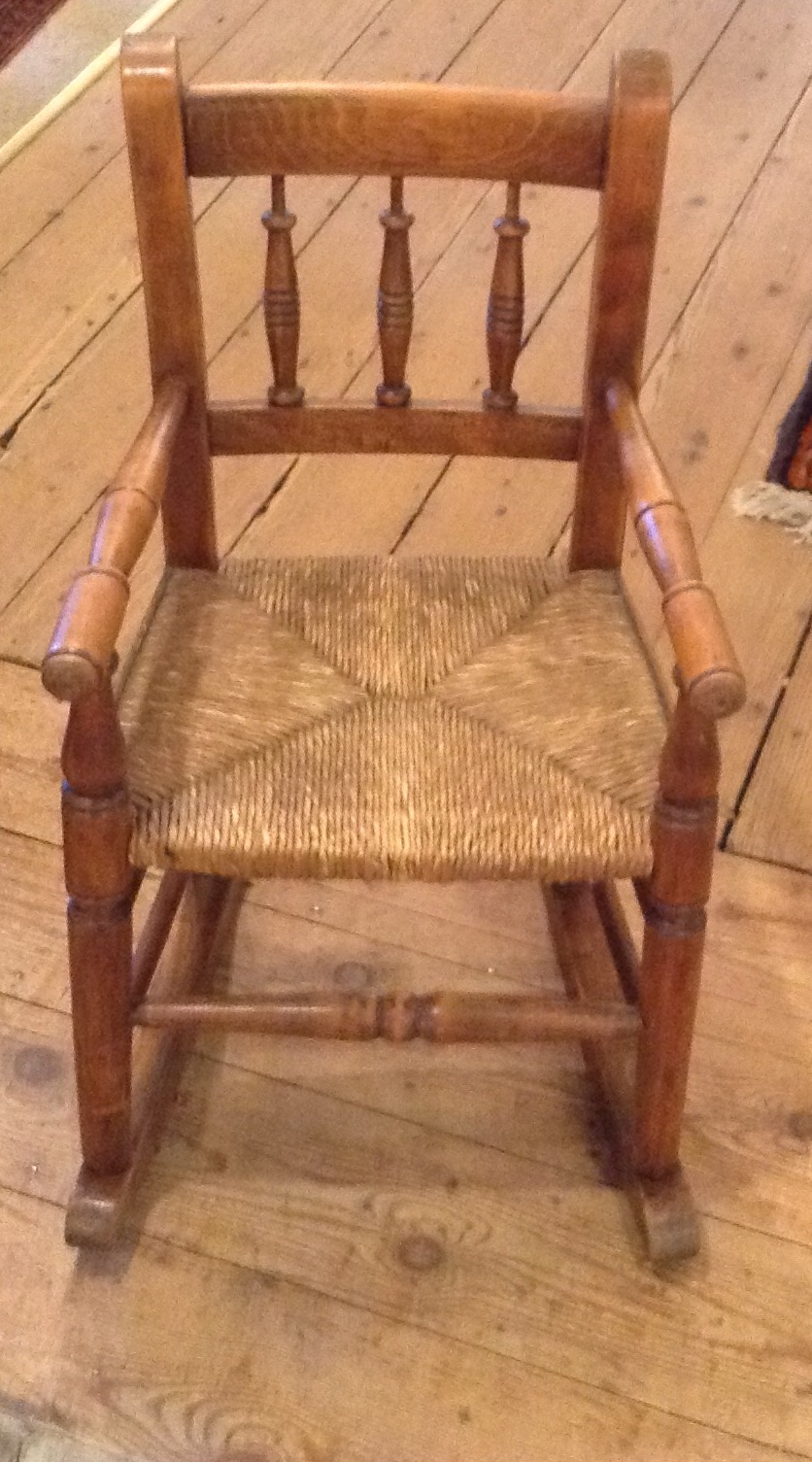 AN EARLY 20TH CENTURY CHILD'S BEECH WOOD ELBOW CHAIR Having a spindle back and rush seat. (approx