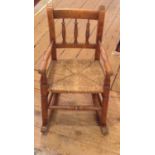 AN EARLY 20TH CENTURY CHILD'S BEECH WOOD ELBOW CHAIR Having a spindle back and rush seat. (approx