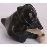 A 20TH CENTURY INUIT DARK GREEN SOFT STONE CARVING  Of an Eskimo hunting, with a bone knife and