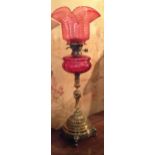 A 19TH CENTURY BRONZE, ORMOLU AND CRANBERRY GLASS OIL LAMP The base cast with flutes, swags and lion