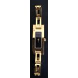 A LADIES' GUCCI YELLOW METAL WRIST WATCH AND STRAP With black rectangular dial, boxed. Condition: