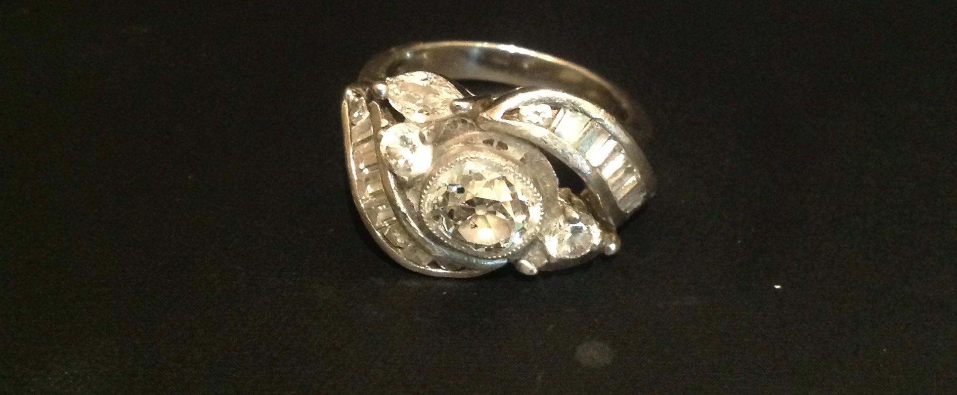 AN UNUSUAL SILVER, DIAMOND AND PASTE SET RING  The central oval brilliant cut diamond collet set and