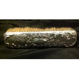 AN EDWARDIAN SILVER CLOTHES BRUSH The silver top embossed with flora and fauna, surrounding a