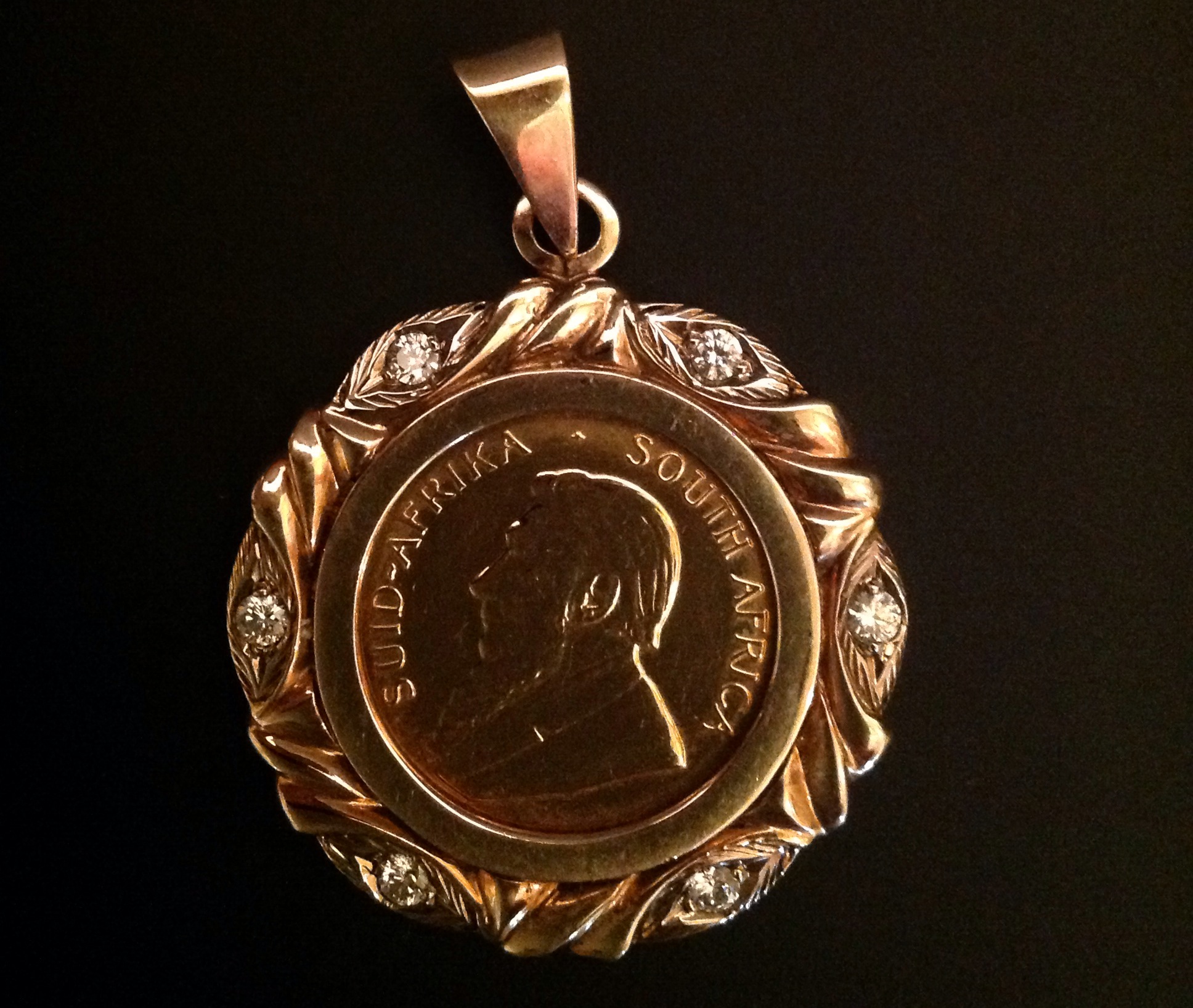 A 22CT GOLD QUARTER KRUGERAND  Mounted in an unmarked gold foliate pendant mount, set with six small