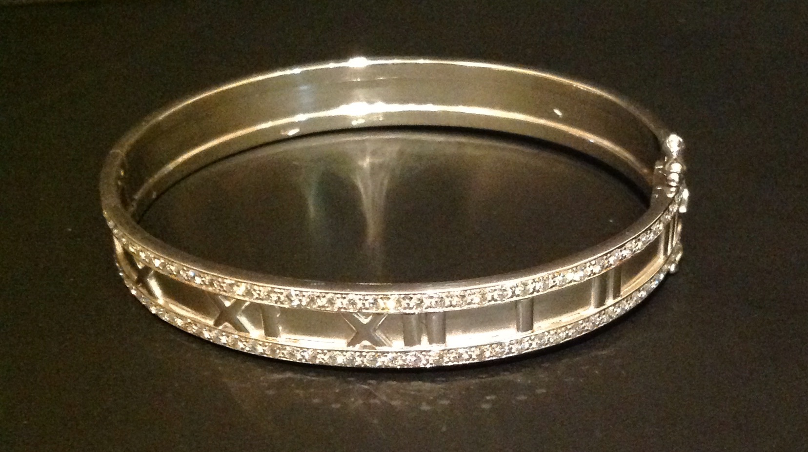 AN 18CT WHITE GOLD AND DIAMOND BANGLE In the style of Cartier 'Atlas', having embossed Roman