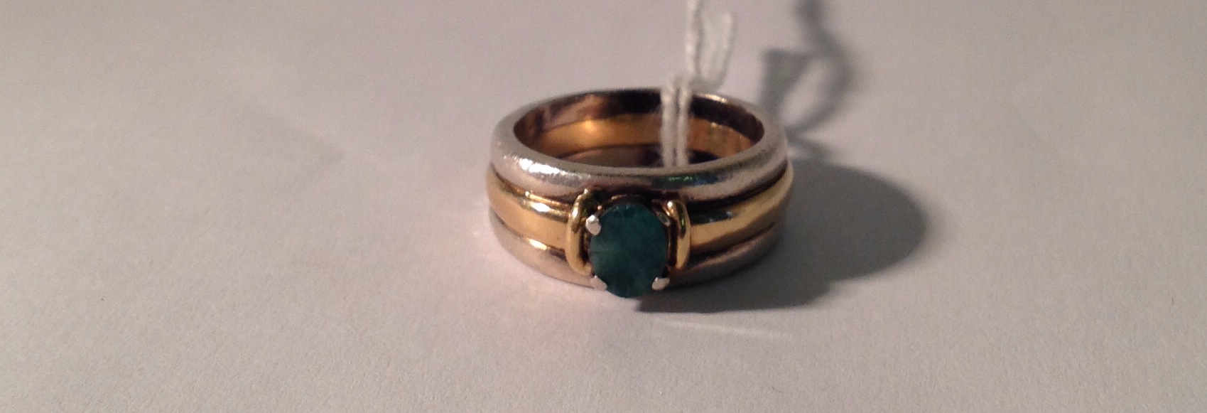 A 9CT GOLD, SILVER AND EMERALD RING The oval brilliant cut emerald set between gold ribs on a 9ct