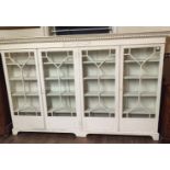 AN EDWARDIAN FLOORSTANDING FOUR DOOR BOOKCASE With a dentil cornice, above an Adams urn and swags