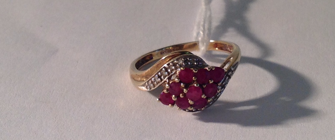 A 9CT GOLD, RUBY AND DIAMOND HALF TWIST RING The nine round brilliant cut rubies arranged in a