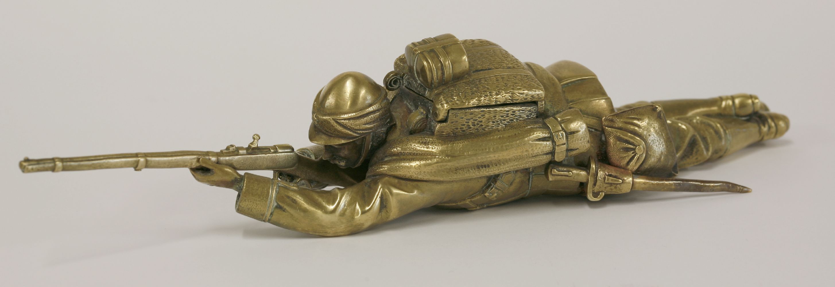 A brass inkwell,c.1900, in the form of a soldier, probably French, lying on his stomach aiming his