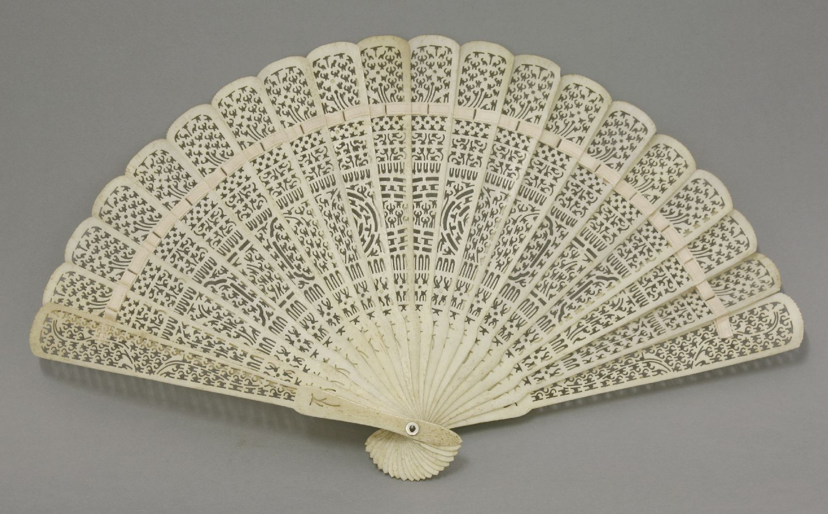 A carved bone Fan, c.1870, intricately pierced with repeating patterns, 32.5cm open, 19cm guard