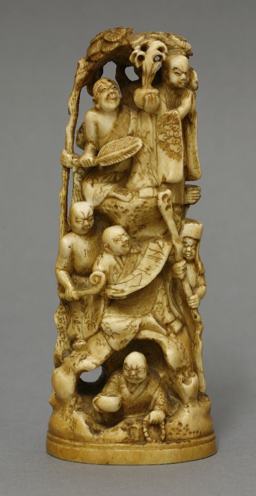 An ivory Okimono, c.1870, carved as eight rakan on a high rock beneath a pine tree, signed Gyokuzan,