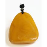 A free-form butterscotch amber pendant,52 x 44 x 17mm, strung on black thread to a piqué work