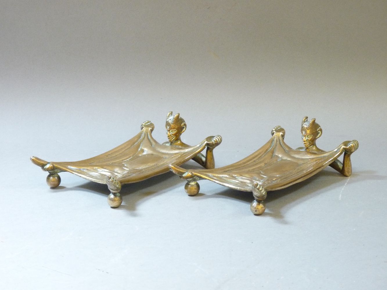 A pair of early 20th century bronze trays, modelled as a devil beneath an outstretched blanket,