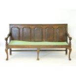 An 18th century oak settle, with panelled back and drop-in seat, on cabriole legs, 182cm wide