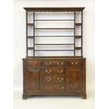 A George III oak Welsh dresser, the open plate rack with wavy frieze above a series of drawers and