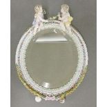 An oval porcelain easel mirror, surmounted with two cherubs, 34cm
