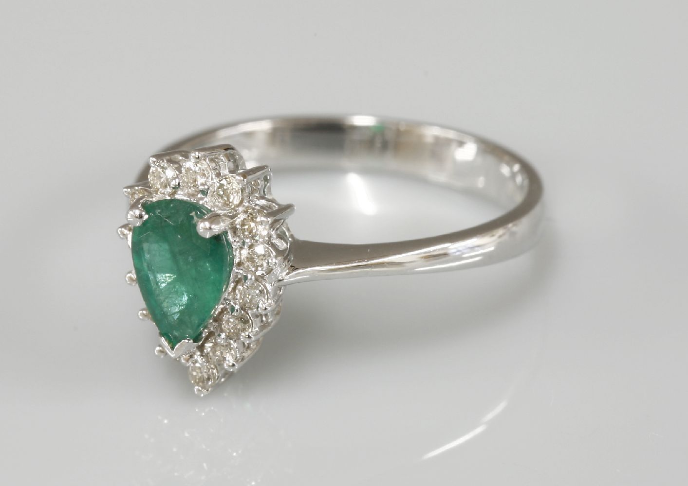 An 18ct white gold pear shaped emerald and diamond cluster ring