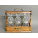 A Victorian oak tantalus, the three bottles with silver wine labels