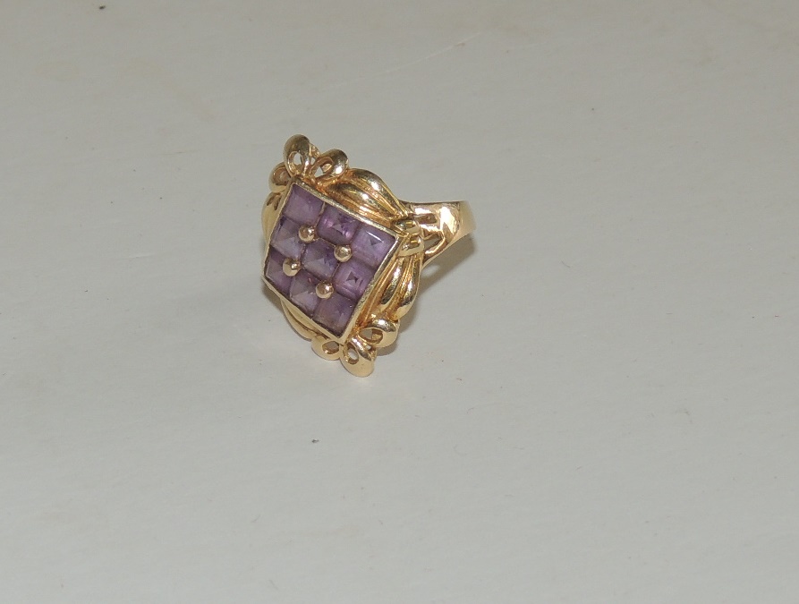 A 14 k gold, ladies dress ring, set with a central panel of nine square cut amethysts, with swag and