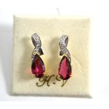 A pair of tourmaline and diamond earrings, a diamond set swirl over a pear cut purplish-red