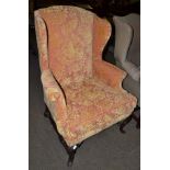 A George II style wing chair on walnut carved legs, joined by a H stretcher