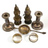 A pair of loaded silver candlesticks, a pair of silver pepperettes, a tea strainer and two napkin