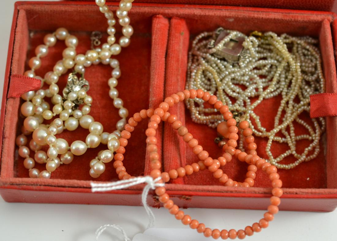 A red jewellery box containing two seed pearl necklaces, a cultured pearl necklace and a coral