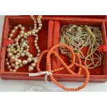 A red jewellery box containing two seed pearl necklaces, a cultured pearl necklace and a coral