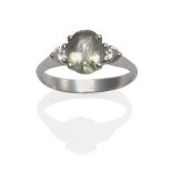 A Green Sapphire and Diamond Ring, the oval cut green sapphire between two round brilliant cut