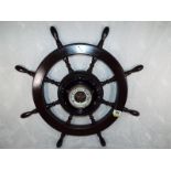 A wall mounted aneroid barometer in the form of a ships wheel, white enamel dial with open centre