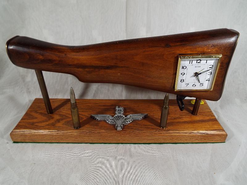 A desk alarm clock in the form of a rifle stock on a wooden pedestal, enhanced by two bullets and