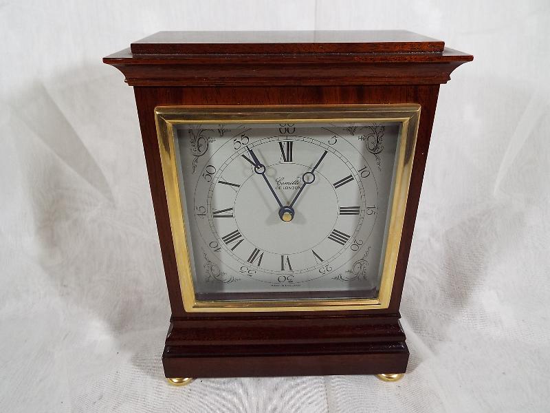 A good mahogany mantel clock by Comitti of London, square white dial with brass bezel, on brass bun