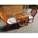 A cane conservatory set comprising oval glass top table and twin chairs