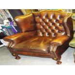 A brown leather button back wing chair with ball and claw feet