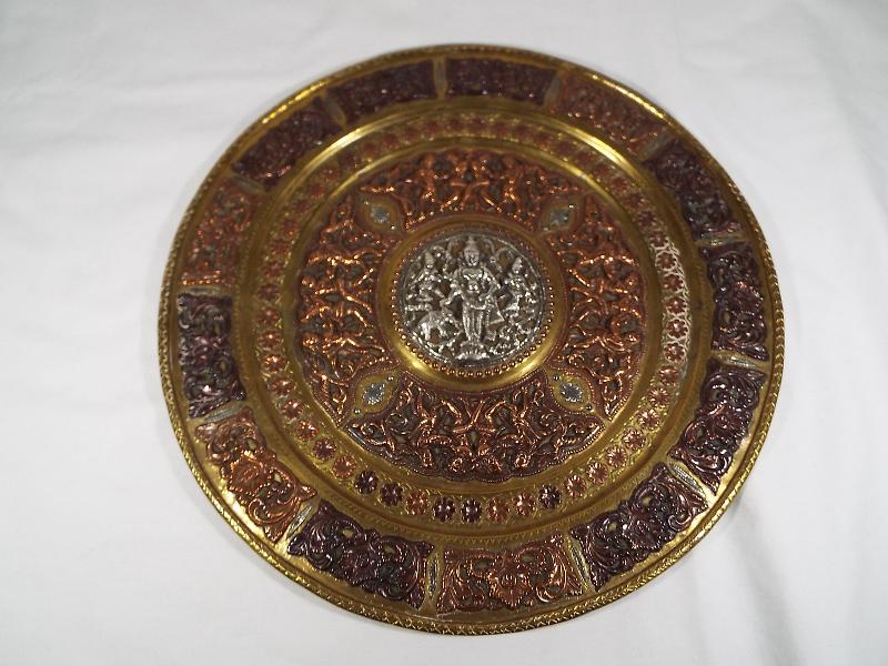 An Indian brass charger with applied copper and silver depictions of figures and foliage,
